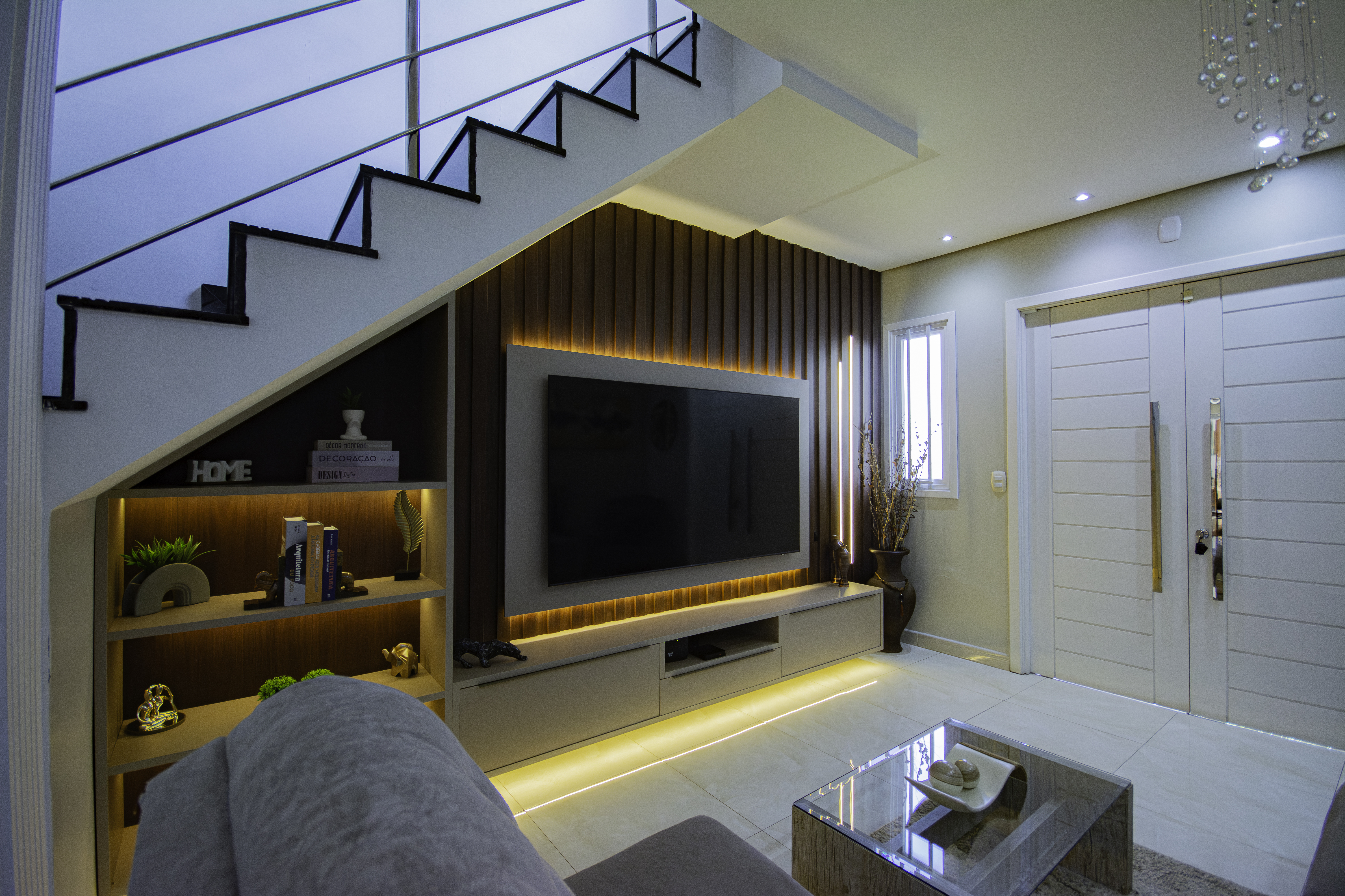 Living moderno com painel de TV sob escada e iluminação cênica